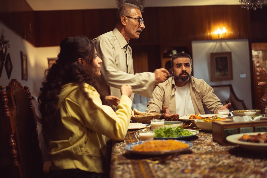 A family enjoys a lively dinner conversation, sharing diverse dishes and drinks at home.