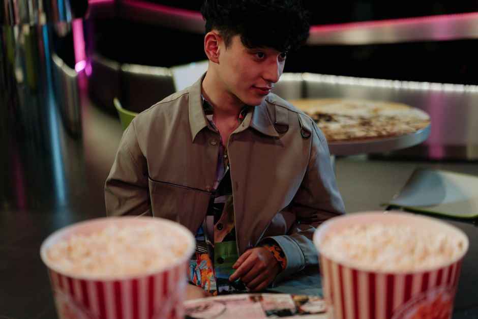 Casual scene of a young man in a cafe, seated with popcorn on the table.
