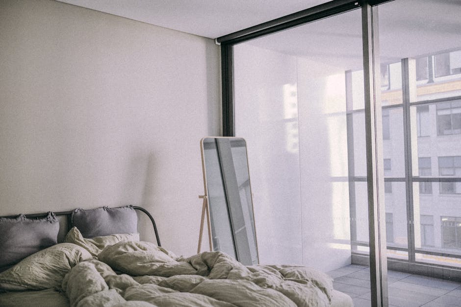 A cozy modern bedroom with minimalistic design, featuring large glass windows and an urban view.