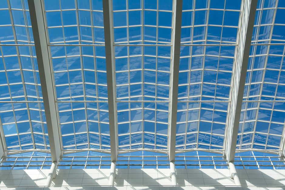Low-angle view of a modern glass ceiling structure against a bright blue sky, showcasing architectural design.