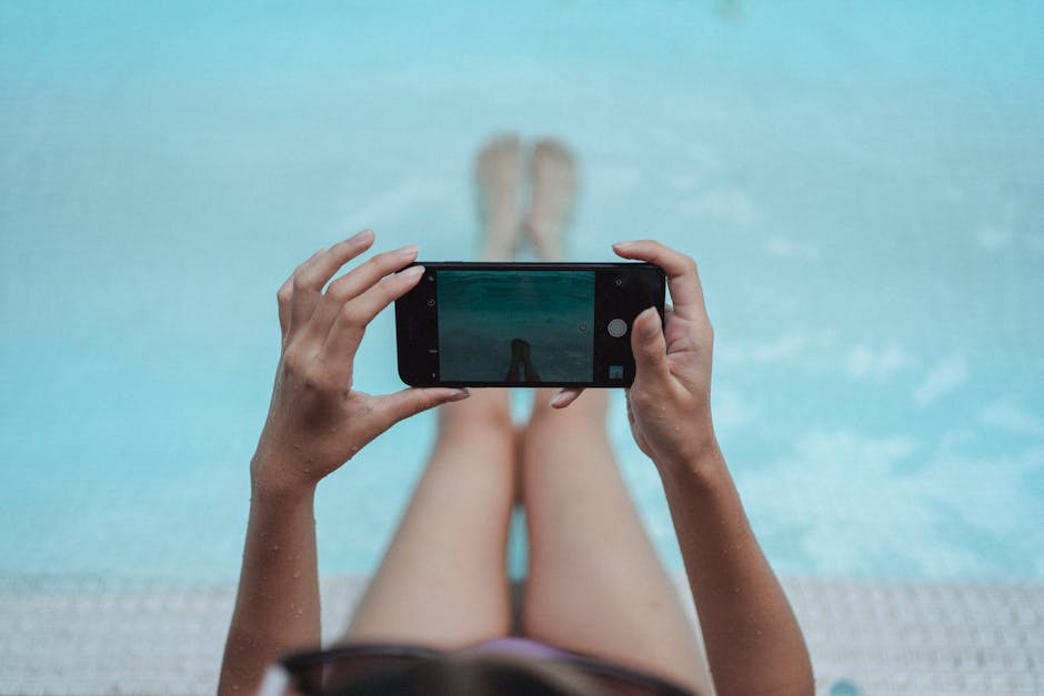 High angle crop anonymous female with fit body relaxing on poolside and taking picture of legs