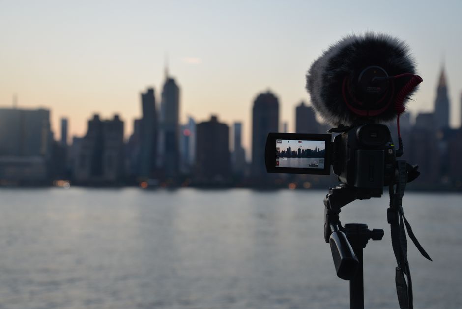 A camera with a microphone captures a city skyline at dawn across a waterfront.