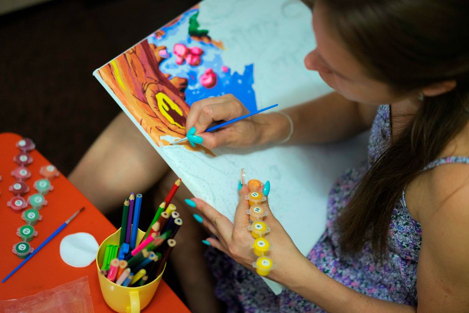 A woman engaged in creative painting with watercolors and brushes on canvas.