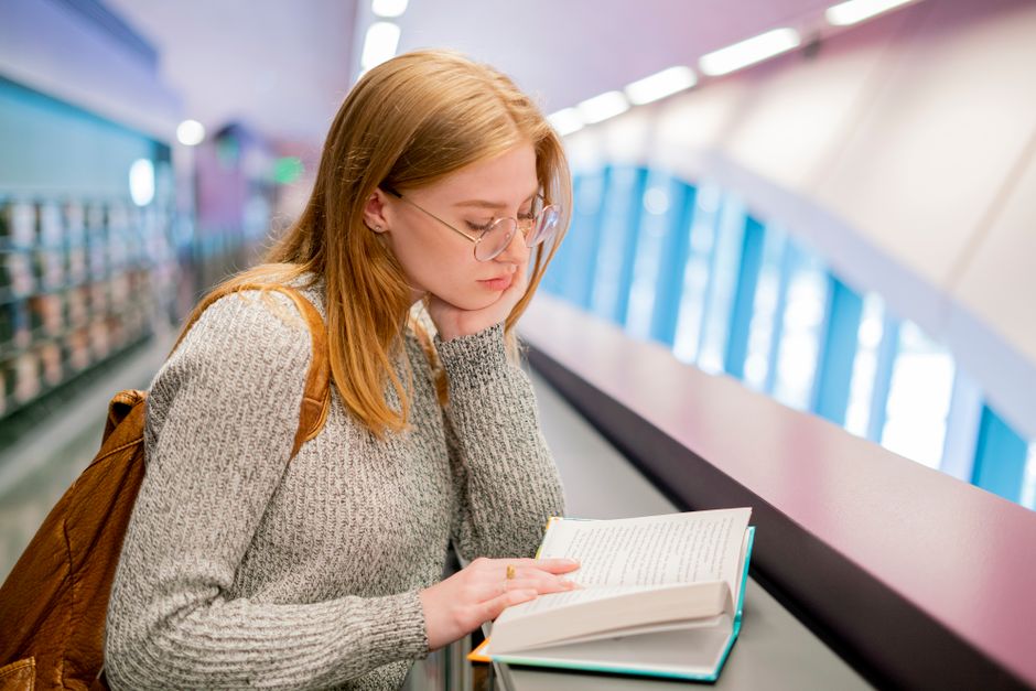A focused young woman reading a book in a bright, modern library environment.
