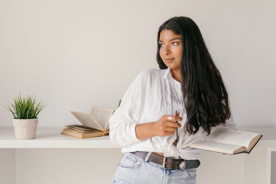 Young woman in casual attire, holding a book, epitomizing focused learning and study.