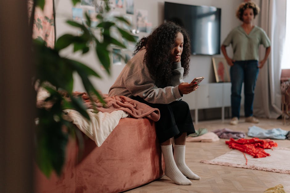 Teen girl uses smartphone while mother stands in colorful, cozy room.