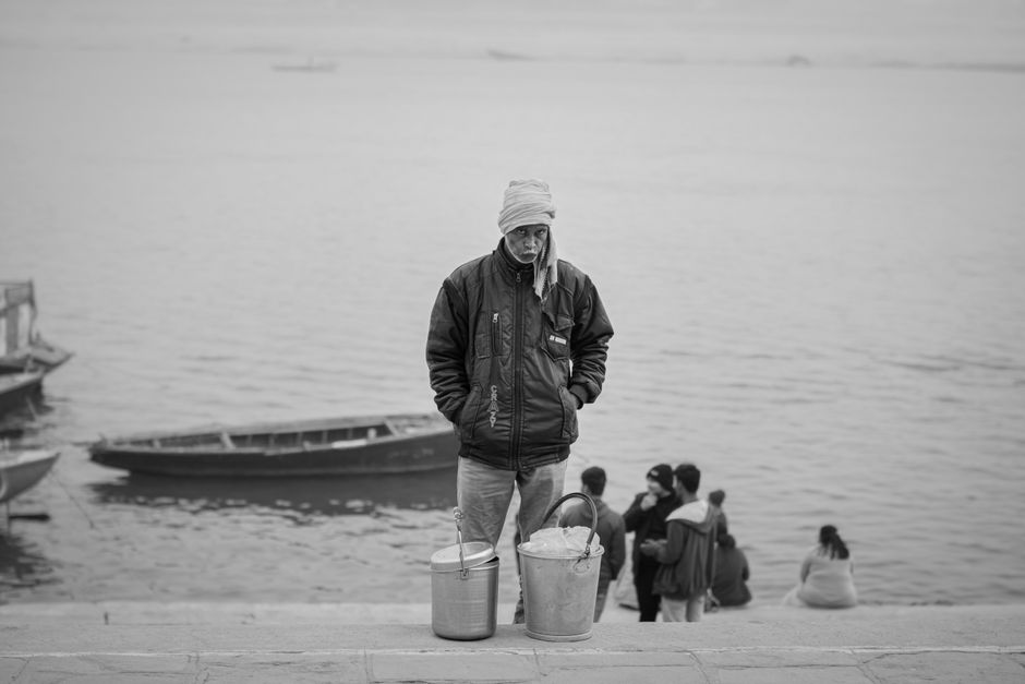Black and white photo of an elderly vendor by the Ganges River in Varanasi, India.