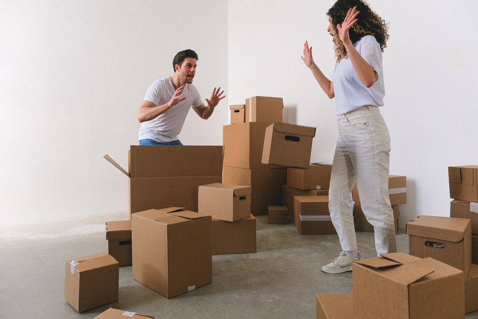 Young couple shouting with hands raised in new apartment with many boxes in daylight