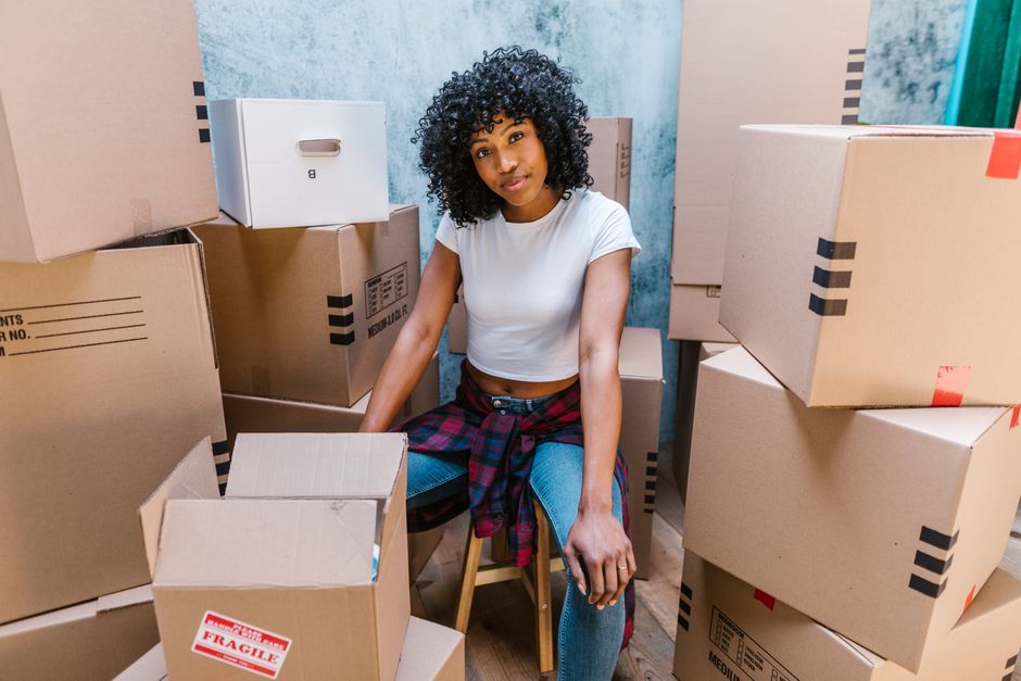 Young woman surrounded by cardboard boxes, preparing for a move or unpacking in her new home.
