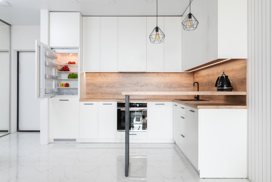 Colorful vegetables in fridge with opened door in modern light spacious kitchen with white furniture and floor