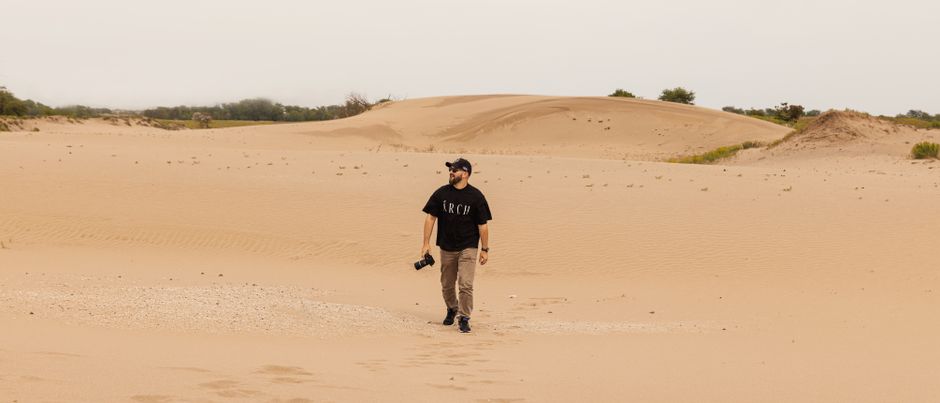 Photographer walking in sandy desert dunes capturing landscapes.