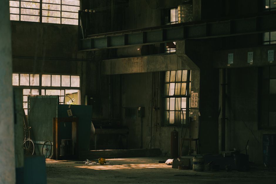 Dark, moody interior shot of an abandoned industrial space with shadows and natural light.