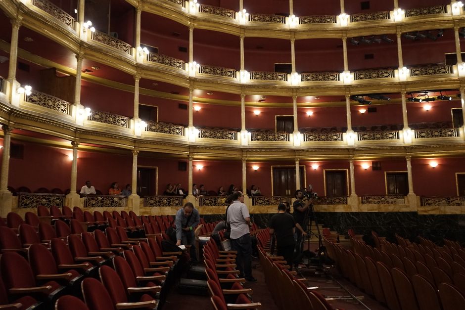 View of a classic theater interior with red seats and a camera crew setting up, capturing the venue's grandeur.
