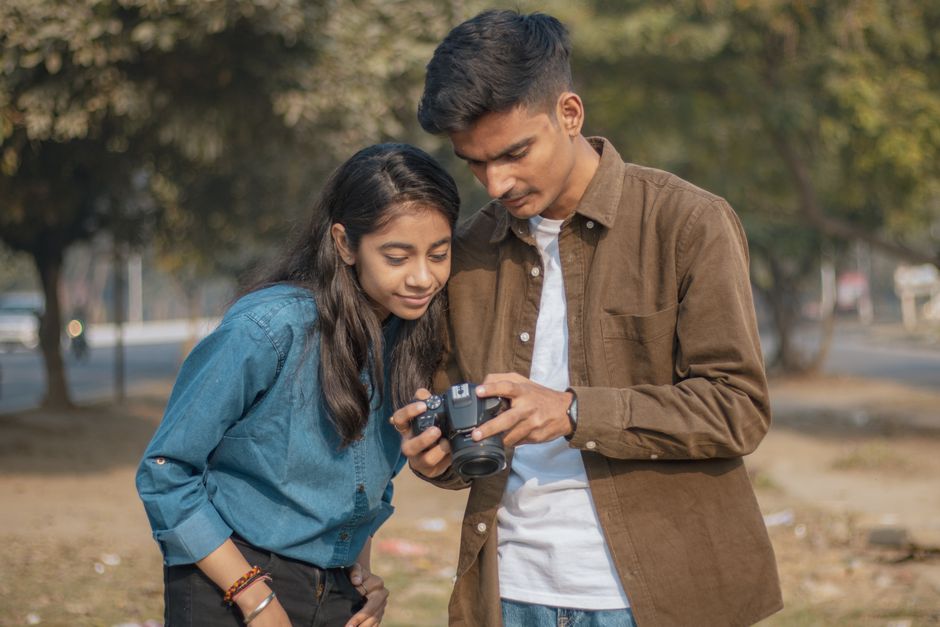 Two young adults reviewing camera shots in a sunny outdoor setting, learning photography skills together.