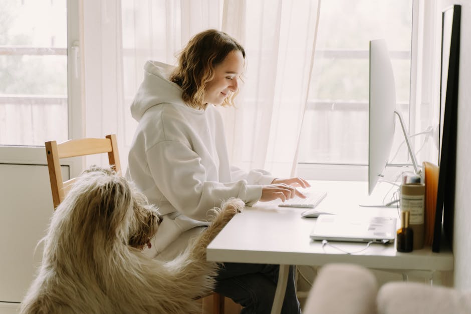 A woman working from home on a computer while her dog sits beside her in a cozy room.