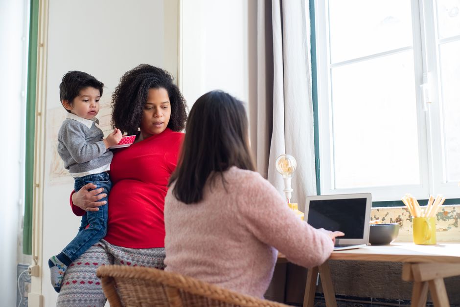 Mother multitasking at home with child while working on a laptop. Warm family atmosphere.