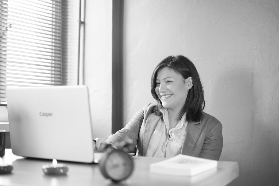 Smiling businesswoman working at her desk with a laptop in a bright office setting.